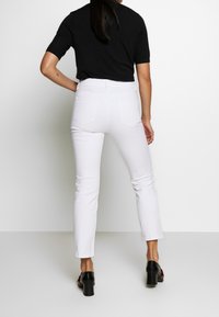 Jeans blancos con un diseño ajustado, cintura de altura media y dos bolsillos traseros. Llevados con una blusa negra de manga corta y zapatos negros de tacón.