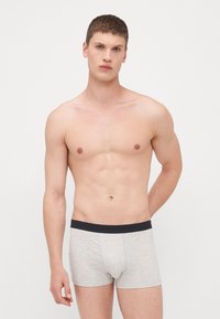Graue Baumwoll-Boxershorts mit einem marineblauen elastischen Bund, die ein enges Design und eine glatte Textur aufweisen. Keine sichtbaren Muster oder Designs.
