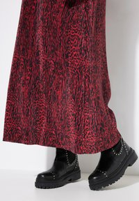 Schwarze Stiefeletten mit einer chunky Sohle, gestuften Akzenten und einer glatten Textur, kombiniert mit einem langen Rock in rot-schwarzem Muster.