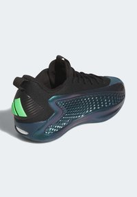 Black athletic shoe with a textured, mesh upper, iridescent accents, and a green design element on the heel. Rounded toe and cushioned sole.