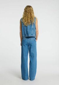 Denim prsluk i široke traperice u svijetloplavoj boji. Prsluk je bez rukava s krojem koji prati tijelo, a traperice imaju visok struk i strašnje džepove.