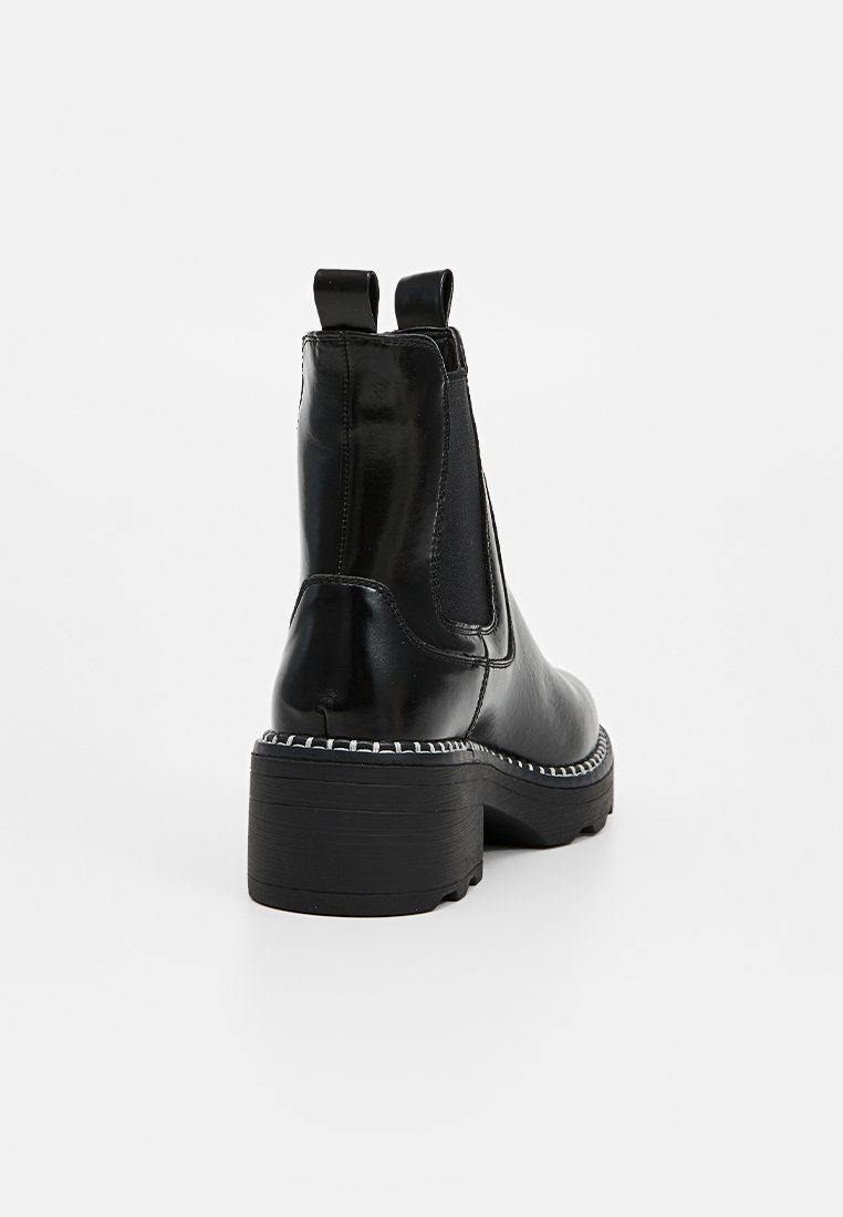 Bottes chelsea noires avec une finition brillante, des panneaux latéraux élastiques et un talon épais. Présente des coutures contrastées le long de la semelle.