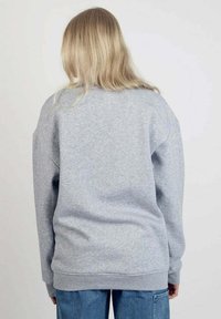 Harmaa huppari, jossa on rento istuvuus, pitkät hihat ja ribattu hihansuu. Kangas tuntuu pehmeältä ja sileältä, eikä siinä ole näkyviä kuvioita tai logoja.