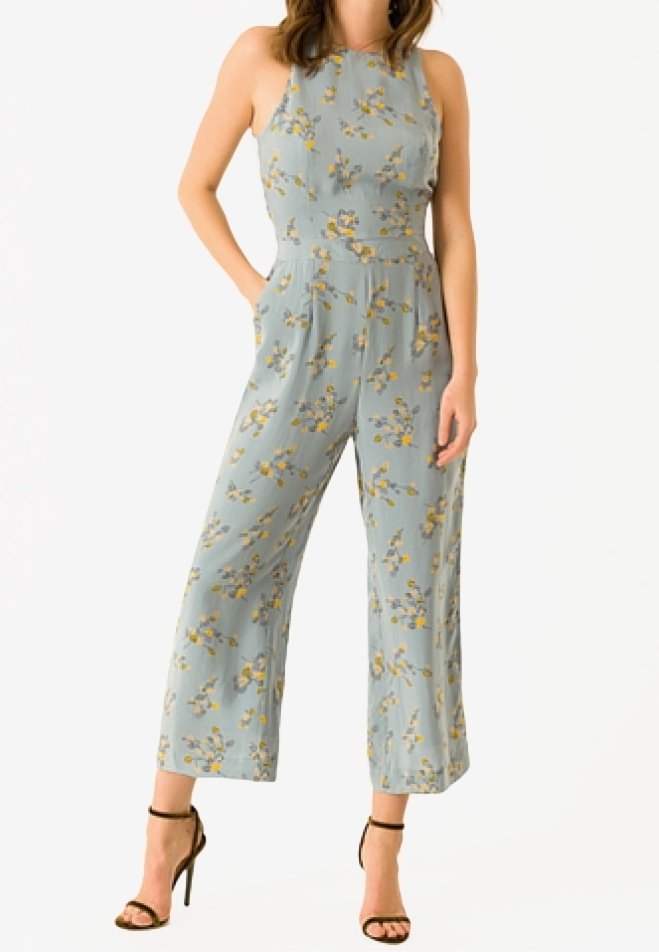 Lyseblå buksedragt med blomsterprint, høj krave, vide ben og sidelommer, med gule og grønne blomster.