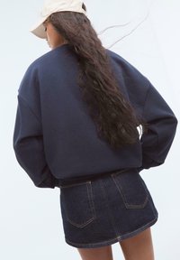Marinvänlig oversized sweatshirts med sjunkna axlar, kombinerad med en mörk denim mini kjol med bakfickor och gula sömmar.