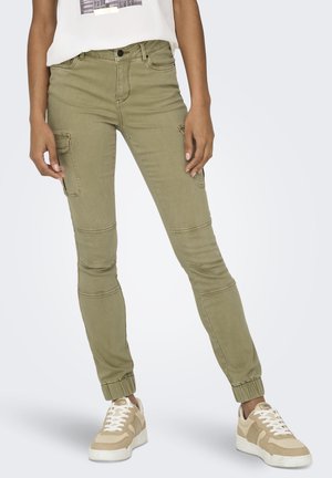 Pantalones cargo de color verde oliva con piernas ajustadas, puños elásticos y múltiples bolsillos, hechos de material de algodón suave. Combinados con zapatillas deportivas claras.
