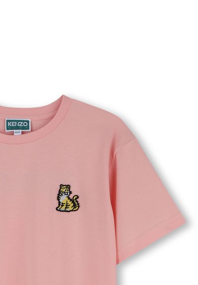T-shirt en coton rose avec un col rond et des manches courtes. Présente un motif de tigre brodé en jaune et noir sur la poitrine gauche.