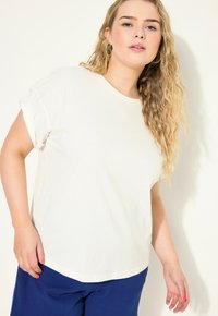 Witte korte mouwen t-shirt met een relaxte pasvorm, voorzien van opgerolde manchetten en een gladde textuur. Gecombineerd met blauwe gestructureerde broek.