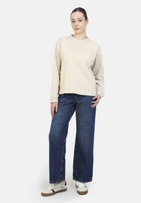 Beige sweatshirt met lange mouwen en een ronde hals, gecombineerd met wijde donkere denim jeans en witte sneakers met zwarte accenten.