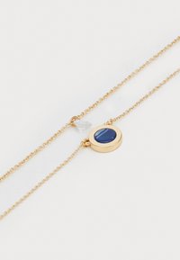 Collana in oro con ciondolo rotondo in pietra blu, con una piccola perlina trasparente vicino al gancio. Design elegante e minimale.