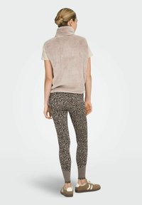 Karvane beež vest kõrge kraega, kombineeritud lillemustriliste pruunide retuusidega ja pruunide spordijalatsitega.