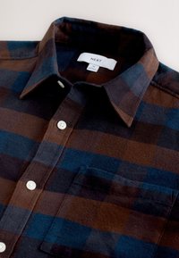 Brązowo-niebieska flanelowa koszula w kratę z kołnierzykiem, zapinana na guziki z kieszenią. Miękka w dotyku, z ozdobnymi guzikami i metką wewnątrz kołnierza.
