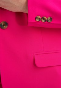 Blazer rosa brillante con textura suave, con un bolsillo en el pecho y cuatro botones marrones en el puño para cierre.