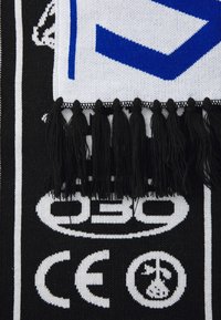Black and white scarf featuring blue geometric design, tassels at the bottom, and printed logos and symbols on the fabric.
