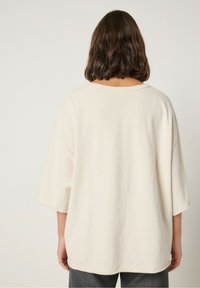 Kremowy, oversize'owy sweter z krótkimi, szerokimi rękawami, okrągłym dekoltem i miękką, fakturowaną tkaniną o luźnym kroju.