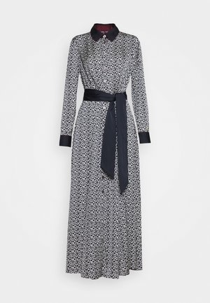 Vestido de manga larga con estampado en blanco y negro, con cuello negro, detalles en los puños, cierre de botones en la parte frontal y cinturón negro para atar a la cintura.