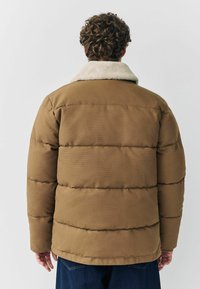 Pruun puhumisjakk koos kreemjast kunstkarvast kraega. Omab tikitud disaini, tekstureeritud kangast ja laia lõiget. Tagakülg näitab varruka pikkust.