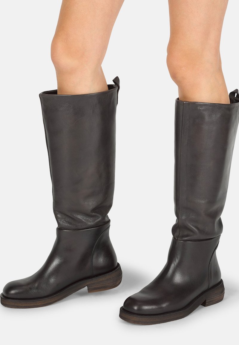 Botas altas de cuero negro hasta la rodilla con punta redondeada y tacón apilado de madera, que presentan un acabado suave y texturizado, además de una tira en la parte superior para facilitar su uso.