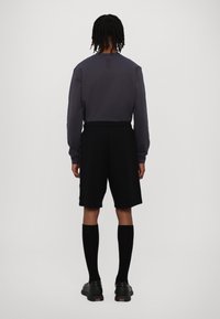 Pantaloni corti neri con una vestibilità rilassata, abbinati a una maglietta a maniche lunghe scura. Indossati con calze nere fino al ginocchio e scarpe nere eleganti.