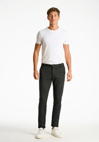Sorte slim-fit bukser med en frontlynlås og knaplukning, parret med en ensfarvet hvid t-shirt med korte ærmer og hvide sneakers.