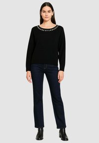 Maglione nero con scollo a girocollo decorato con piccoli abbellimenti, abbinato a jeans blu scuro e stivaletti neri.