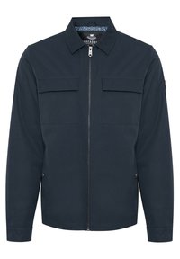 Marineblå lynlåstrøje med spids krave, to brystlommer med klap, lange ærmer og lommer med knapper i siden.