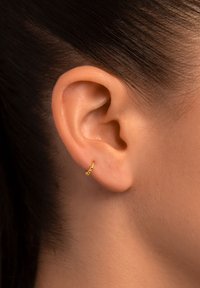 Pendiente de aro dorado con un pequeño diseño en espiral, que presenta un acabado pulido y acentos texturizados. Lleva puesto en un primer plano de una oreja.
