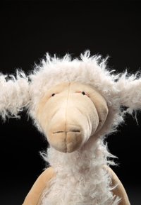 Plush sheep toy with a beige body, fluffy white head and ears, stitched facial features, and textured wool-like fabric.
