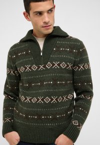 Zelený pletený sveter s polovičným zipsom na golieri, zdobený geometrickými vzormi v krémovej a vínovej farbe. Rebrované manžety a lem, vlnená textúra.