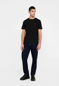 Sort bomuld kortærmet t-shirt med rund halsudskæring og et lille logo på brystet, kombineret med mørke denimjeans og sorte sneakers.