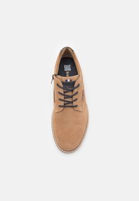 Zapato de ante marrón con cordones, punta redondeada, cordones oscuros en contraste y una lengüeta texturizada. Presenta una suela blanca cosida y un detalle del logo.