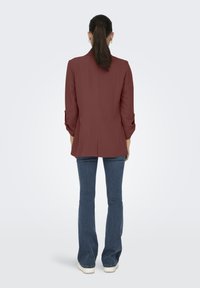 Bordeaux blazer met lange mouwen, getailleerde pasvorm, enkele vent aan de achterkant, gecombineerd met-uitlopende blauwe jeans en witte sneakers.