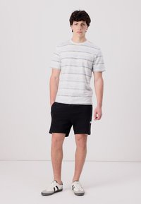 Gråstripet t-skjorte med korte ermer kombinert med svarte shorts. Antrekket fullføres med grå og svarte joggesko.