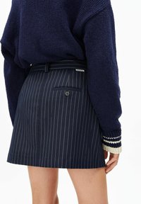 Marineblauer Rock mit Nadelstreifen und maßgeschneidertem Schnitt, ausgestattet mit einer Gesäßtasche und Knopfdetail, kombiniert mit einem strukturierten marineblauen Pullover mit gestreiften Bündchen.