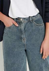 Lichtblauwe denim high-waisted jeans met een rechte pijp, voorzien van contrasterende oranje stiksels, een metalen knoopsluiting en zijzakken.