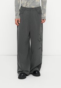 Pantaloni largi gri cu dungi, cu un design brodat pe o parte, având închidere cu nasture și buzunare laterale. Textură de stofă moale.