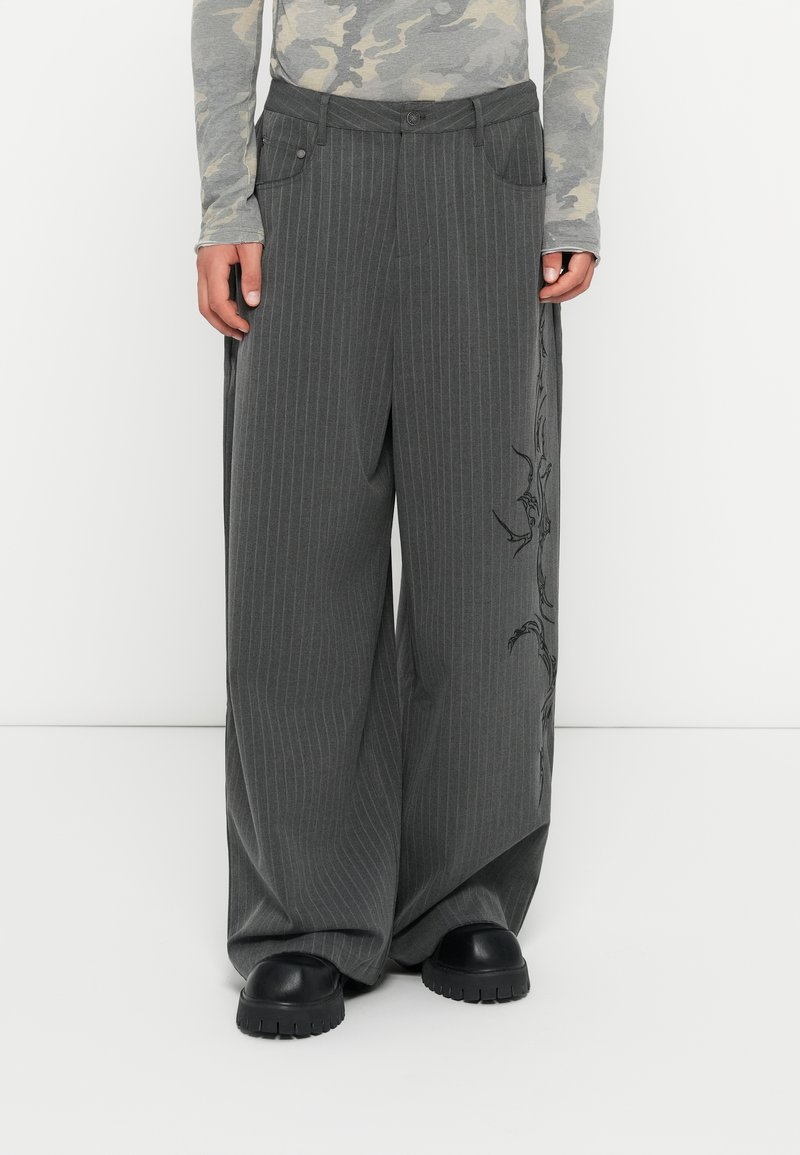 Pantaloni largi gri cu dungi, cu un design brodat pe o parte, având închidere cu nasture și buzunare laterale. Textură de stofă moale.