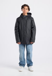 Black waterproof jacket with a hood, featuring snap buttons, worn over light blue loose-fitting jeans and white sneakers.