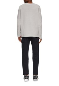 Graues, strukturiertes Langarmshirt, präsentiert an einem Model, kombiniert mit schwarzen Cargo-Hosen mit Seitentaschen und schwarzen und weißen Sneakers.