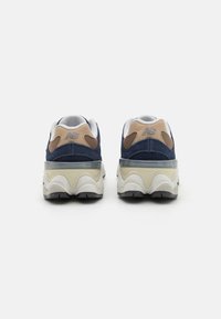 Sneaker in suede blu navy e beige con dettagli bianchi, dotate di collo imbottito, pannelli in mesh testurizzato e suola chunky bianca e grigia.