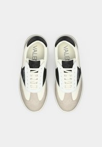 Baskets avec une tige en cuir crème, des accents noirs et des détails en daim gris. Elles sont dotées de lacets blancs et d'un design à bout arrondi.