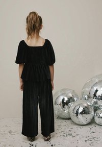 Czarna aksamitna bluzka z bufkami i plisowanym wzorem, w połączeniu z szerokimi spodniami w kolorze czarnym. Półbuty w panterkę, otoczone refleksyjnymi kulami dyskowymi.