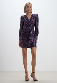 Abito mini viola con scollatura a V, maniche lunghe a palloncino e un motivo astratto nero; presenta un davanti drappeggiato e un orlo asimmetrico.