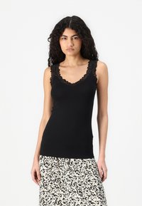 Black tank top with lace trim along the neckline and shoulders, made from a soft material. Worn with a patterned skirt featuring a light color scheme.
