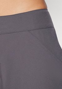 Mørkegrå treningsbukser med høy midje, teksturert stoff, skrå sømdetaljer og glatt, elastisk materiale.