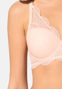 Spetsbh i mjuk rosa, med vågig kant, vadderade kupor och intrikata spetsdetaljer på axelbanden för extra textur och visuell intresse.