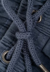 Primer plano de un cordón azul tejido atado en un nudo simple a través de ojales metálicos sobre tela texturizada.