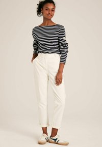 Námornícke a biele pruhované tričko s dlhým rukávom a lodičkovým výstrihom, skombinované s bielymi nohavicami s manžetami a textúrovanými teniskami s modrými akcentmi.