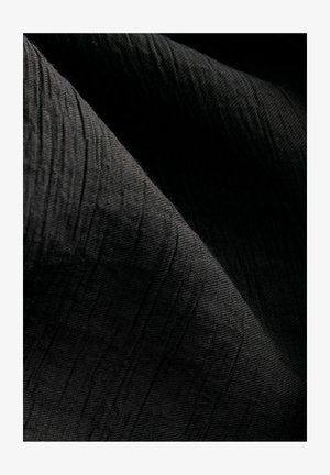 Texturiertes schwarzes Gewebe mit einem subtilen gerippten Muster, leicht reflektierend, das in Falten fällt und seine Tiefe sowie taktile Qualität verstärkt.