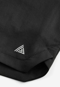 Svart tyg med söm och en liten vit triangulär geometrisk logotyp nära kanten.